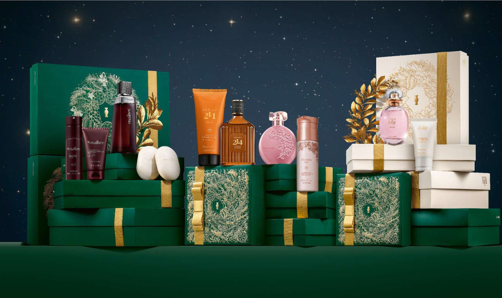Embalagens de Natal do Boticário em tons de verde e dourado, com kits sofisticados dispostos em cenário iluminado, transmitindo elegância e clima festivo